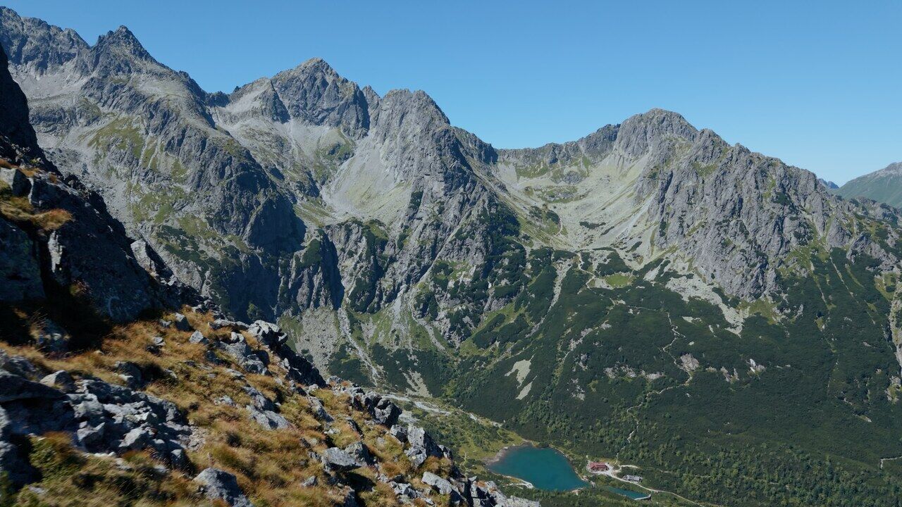 A mountain range with a small alpine lake in the valley below and a rocky ridgeline in the foreground.