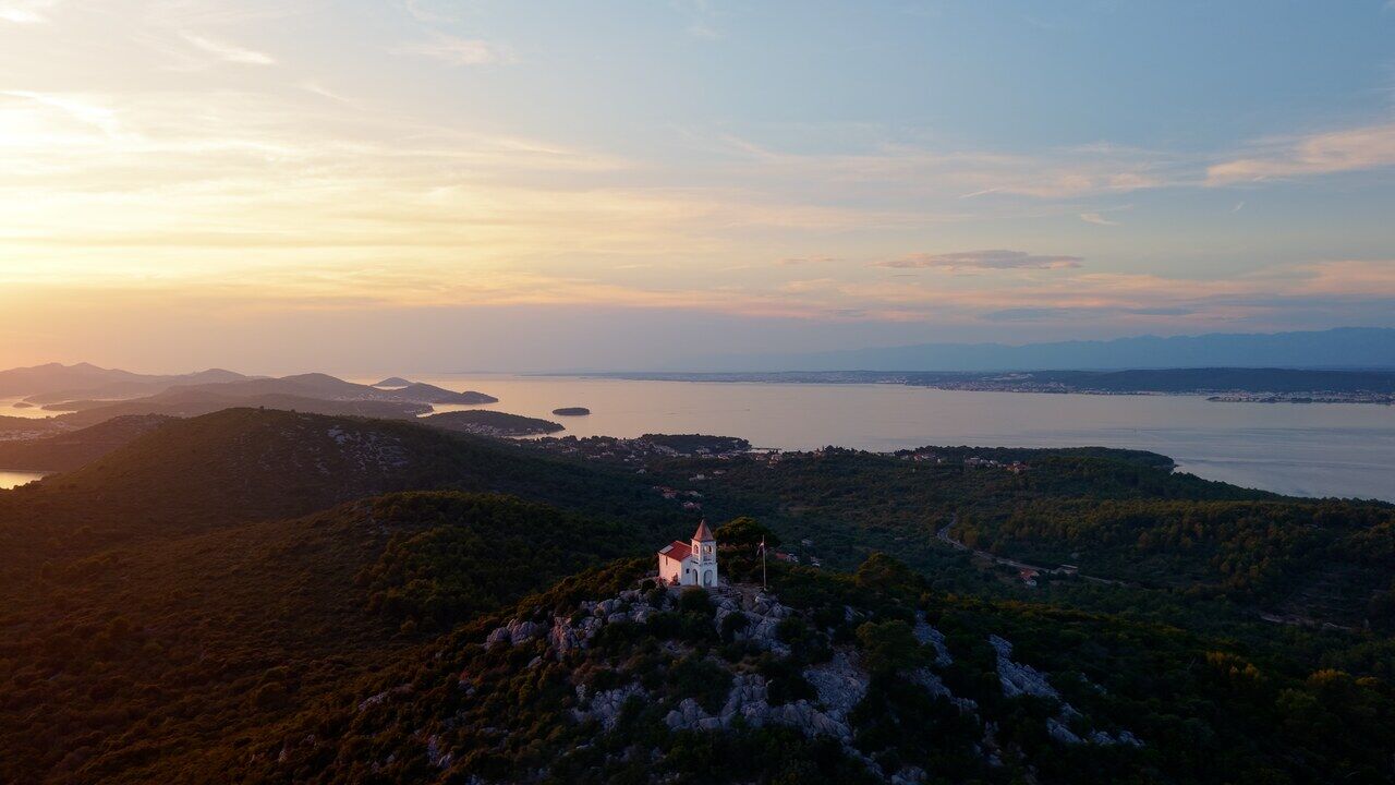 A coastline in low golden light, with a hilltop building silhouetted above islands out in the sea.