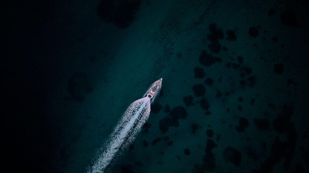 A boat cutting a white wake across dark turquoise water, seen from directly overhead.